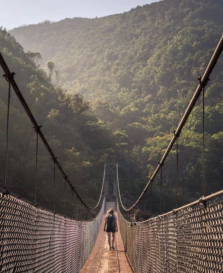 A woman walks across a suspension bridge at Storms River Mouth, South Africa